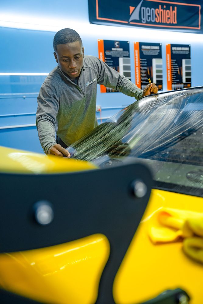 A man is cleaning the windshield of a yellow car.