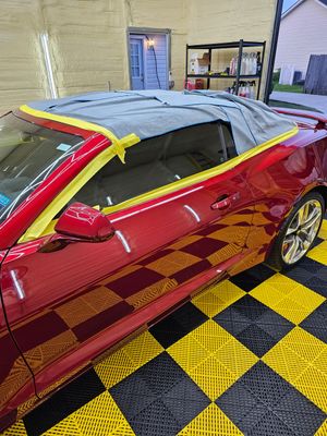 A red convertible car is sitting on a checkered floor in a garage.