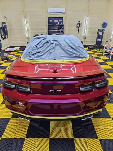 A red car is sitting on a checkered floor in a garage.